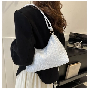 Détail du sac plissé blanc avec bandoulière nouée et anneau métallique doré élégant