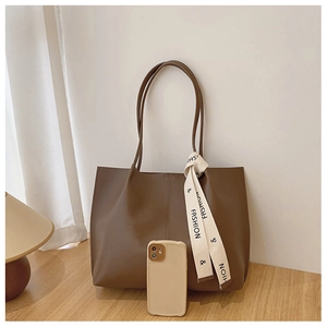 Detail of dark brown matte leather tote bag with fashion ribbon and phone for scale