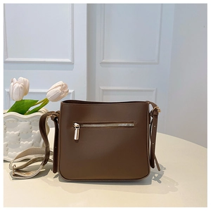 Detail of dark brown leather crossbody bag with dual straps and silver zipper on white table