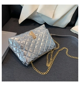 Detail of silver quilted crossbody bag featuring golden T-lock and chain strap on dark fabric