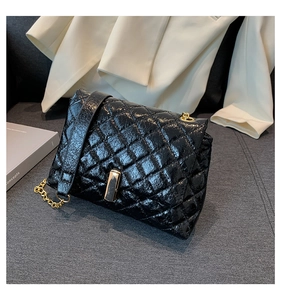 Detail of black quilted patent leather shoulder bag with golden chain and metal lock