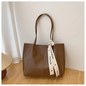 Detail of a brown tote bag featuring vertical stitching and a fashion ribbon strap accessory