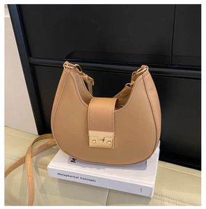 Detail of light brown hobo bag with golden metal press lock on a decorative book