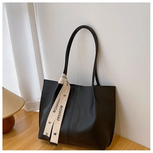 Detail of black leather tote bag featuring vertical stitching and a fashion silk scarf handle