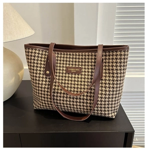 Close-up of houndstooth tote bag fabric with leather handles and brand logo tag