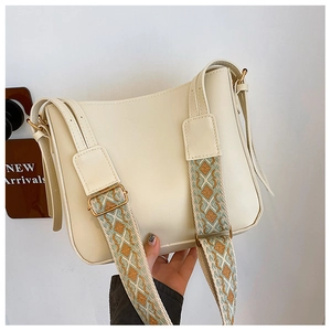 Detail of cream crossbody bag featuring wide colorful jacquard straps and gold hardware