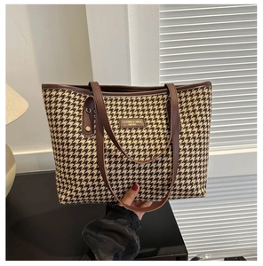 Detail of houndstooth tote bag showing leather handles and gold brand label