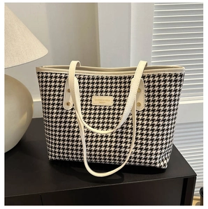 Macro view of houndstooth weave pattern and cream leather trim with gold studs on tote bag