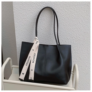Detail of black tote bag featuring a decorative cream ribbon with FASHION text