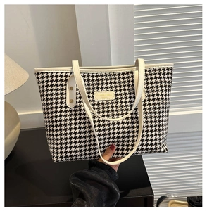 Detailed close-up of classic houndstooth weave texture and leather handle on a tote bag