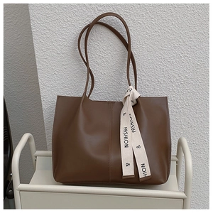 Detail of a brown tote bag featuring decorative silk ribbon and vertical seam stitching