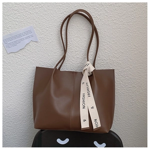 Detail of a brown matte leather tote bag featuring a stylish printed fashion ribbon strap