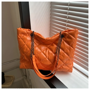Gros plan sur la texture matelassée orange vif et la bandoulière en chaîne de ce grand sac