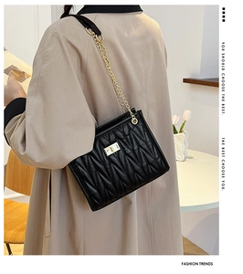 Detail of black quilted shoulder bag with gold metal twist lock and chain strap on model