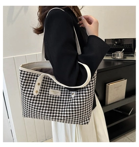 Detail of classic houndstooth tote bag with white leather handle and metal logo plaque