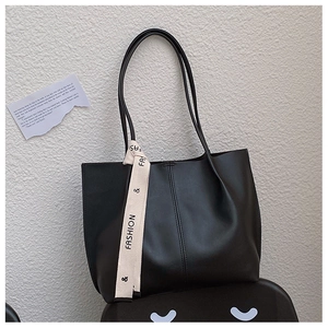 Close-up of black leather tote bag featuring a decorative beige ribbon with fashion text
