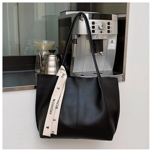 Detail of black faux leather tote bag with a cream ribbon strap showing texture and stitching