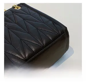 Close-up of black V-quilted faux leather bag with gold metal chain eyelet details
