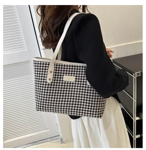 Close-up of black and white houndstooth tote bag featuring white leather straps and gold rivets