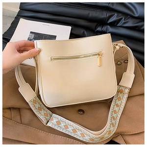 Detail of cream crossbody bag with patterned wide strap on a brown coat background