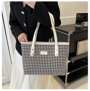 Close-up of houndstooth tote bag with leather handles and metallic rivet details