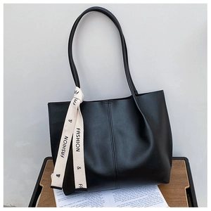 Detail of minimalist black tote bag with vertical stitching and cream ribbon decoration