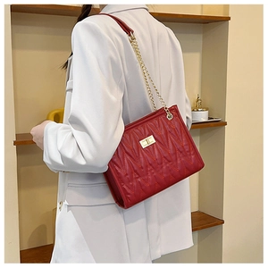 Detail of red quilted leather shoulder bag featuring golden lock and elegant chain strap