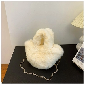 Gros plan du sac seau en peluche blanche avec bandoulière chaîne dorée sur table