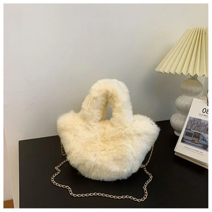 Gros plan du sac seau en peluche crème avec bandoulière dorée sur un bureau noir