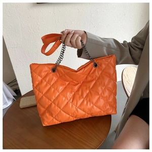 Détail macro d'un sac cabas orange matelassé avec chaîne gris foncé sur une table en bois