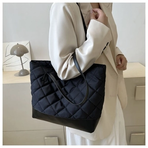 Dettaglio di una borsa tote trapuntata nera indossata da una modella con un blazer beige