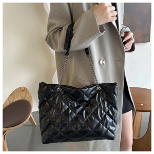 Détail d'un grand sac cabas noir matelassé avec bandoulière chaîne porté dans un cadre minimaliste