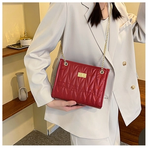 Detail of red quilted leather crossbody bag with gold chain strap and metal lock buckle