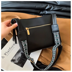 Detail view of black crossbody bag with wide green geometric jacquard strap and gold zipper