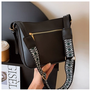 Detail of black crossbody bag featuring a wide geometric ethnic strap and golden zipper