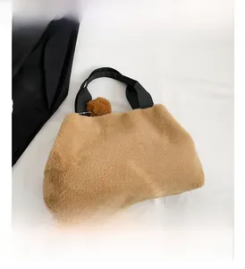 Detail view of brown plush faux fur handbag with black wide handle and fluffy ball charm