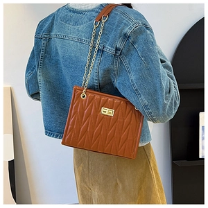 Detailed view of brown quilted tote with gold chain strap on model's shoulder