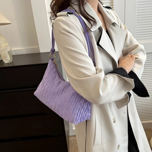 Sac à bandoulière plissé violet avec texture verticale et détails dorés sur manteau blanc