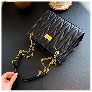 Detail of black quilted shoulder bag with golden twist lock and metal chain strap