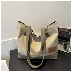 Dettaglio di borsa tote in tela beige e verde oliva accanto a un laptop su un tavolo