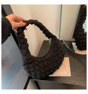 Detail of black bubble texture handbag with gold zipper and minimalist pleated design