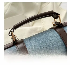 Detail of blue denim fabric with dark brown leather handle and gold metal hardware buckles