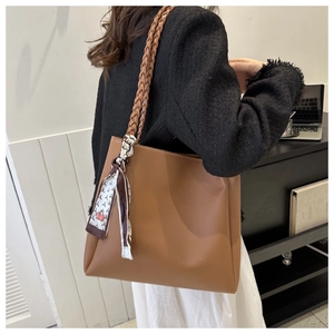 Brown leather tote bag featuring a woven shoulder strap and decorative silk scarf detail