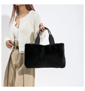 Detail of a fluffy black faux fur tote bag with a matching plush pom-pom charm