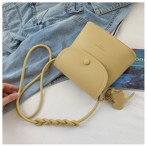 Close-up of yellow pebble leather crossbody bag with braided strap and elephant charm