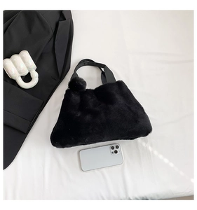 Flat lay detail of black plush bucket bag with fuzzy pompom and soft faux fur texture