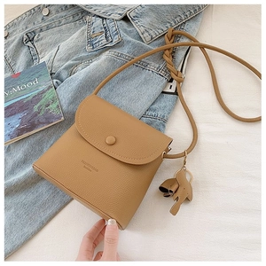 Detail of khaki crossbody bag with elephant charm and woven strap on fashion background