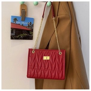 Detail of red quilted leather bag featuring V-shaped texture and gold chain strap