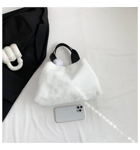 Top-down view of white faux fur bucket bag with black handles and plush ball charm detail