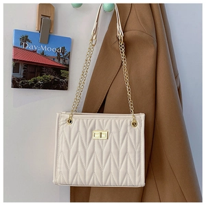 Detail of cream quilted crossbody bag with gold chain strap and turn-lock closure